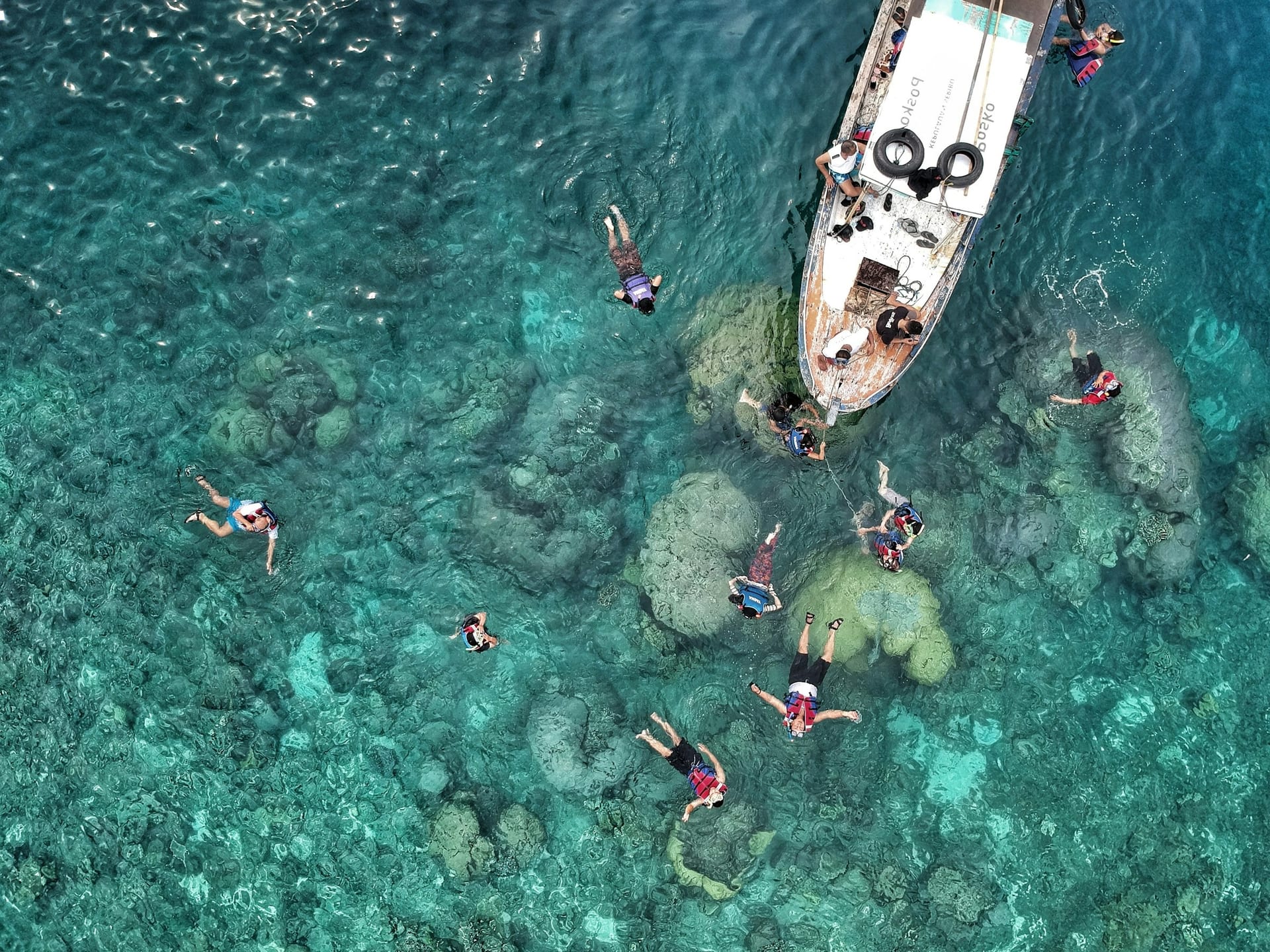 Aerial view of people snorkelling in clear turquoise water beside a boat